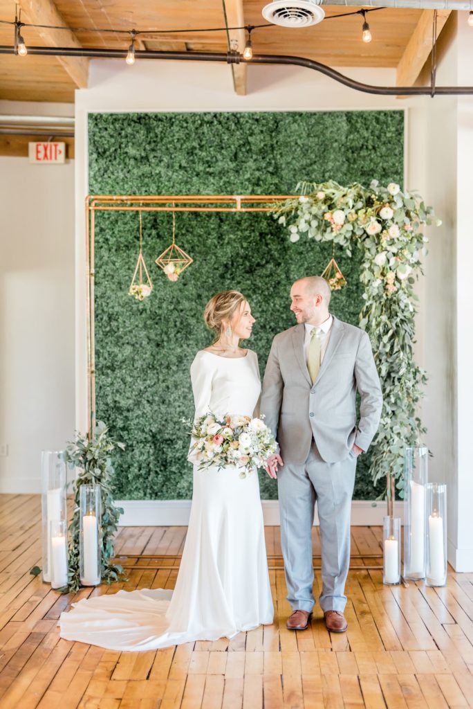 bride and groom in front of boxwood wall at Baker Lofts